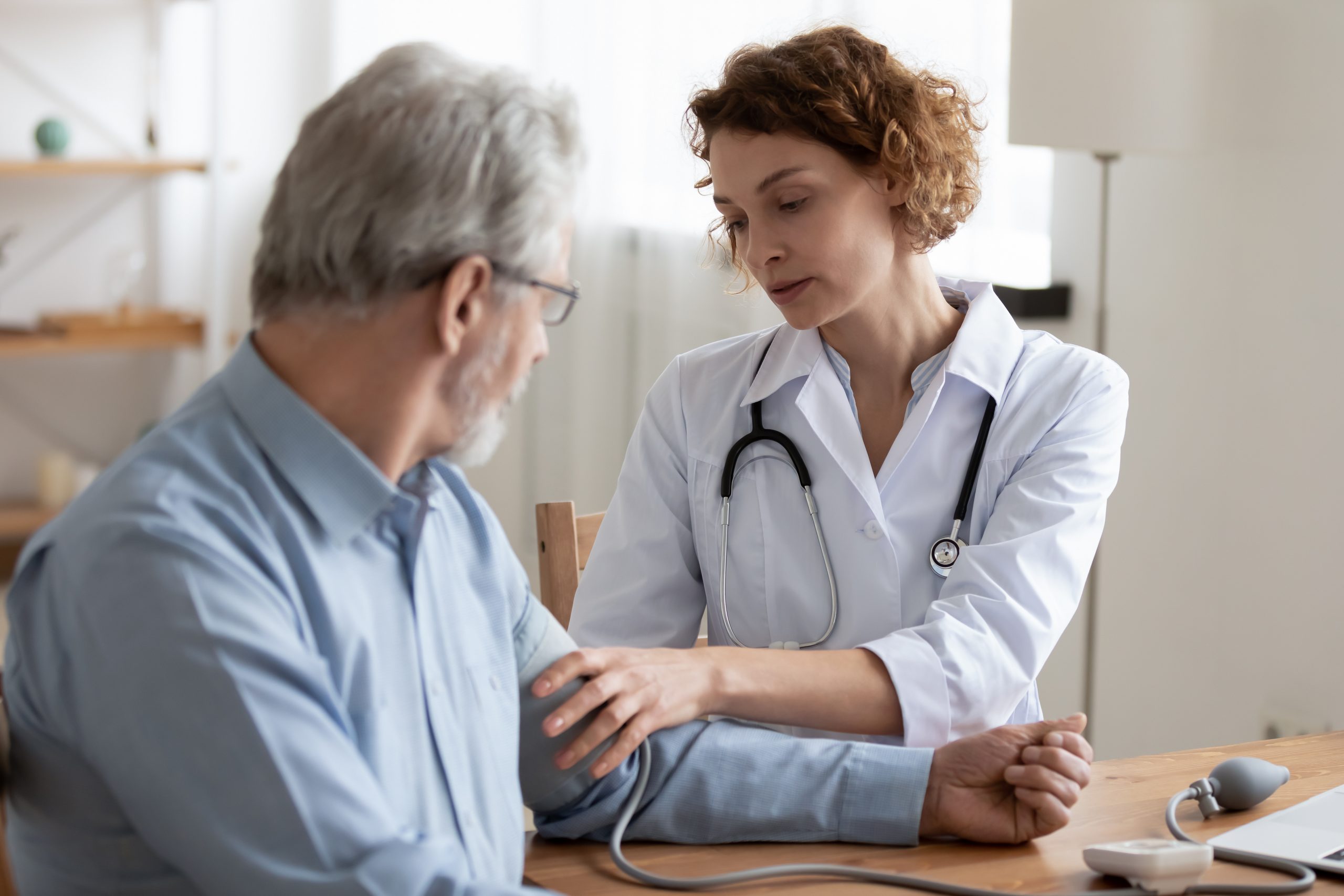Young woman doctor checking mature patient blood pressure at meeting