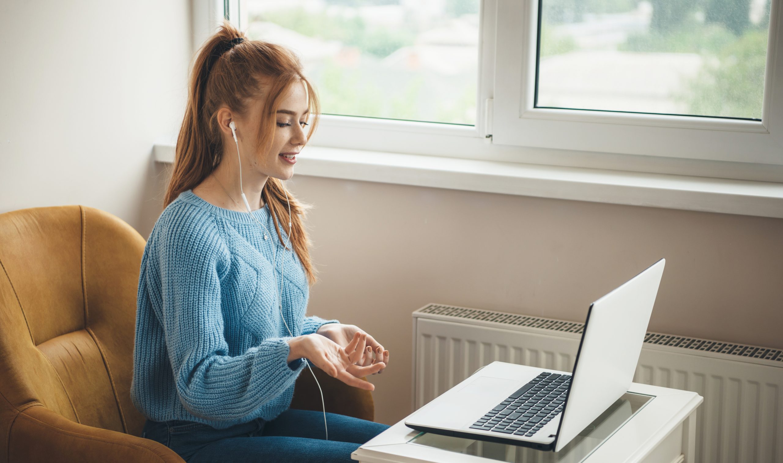 Side view photo of a caucasian woman with red hair and freckles explaining something at laptop wearing earphones